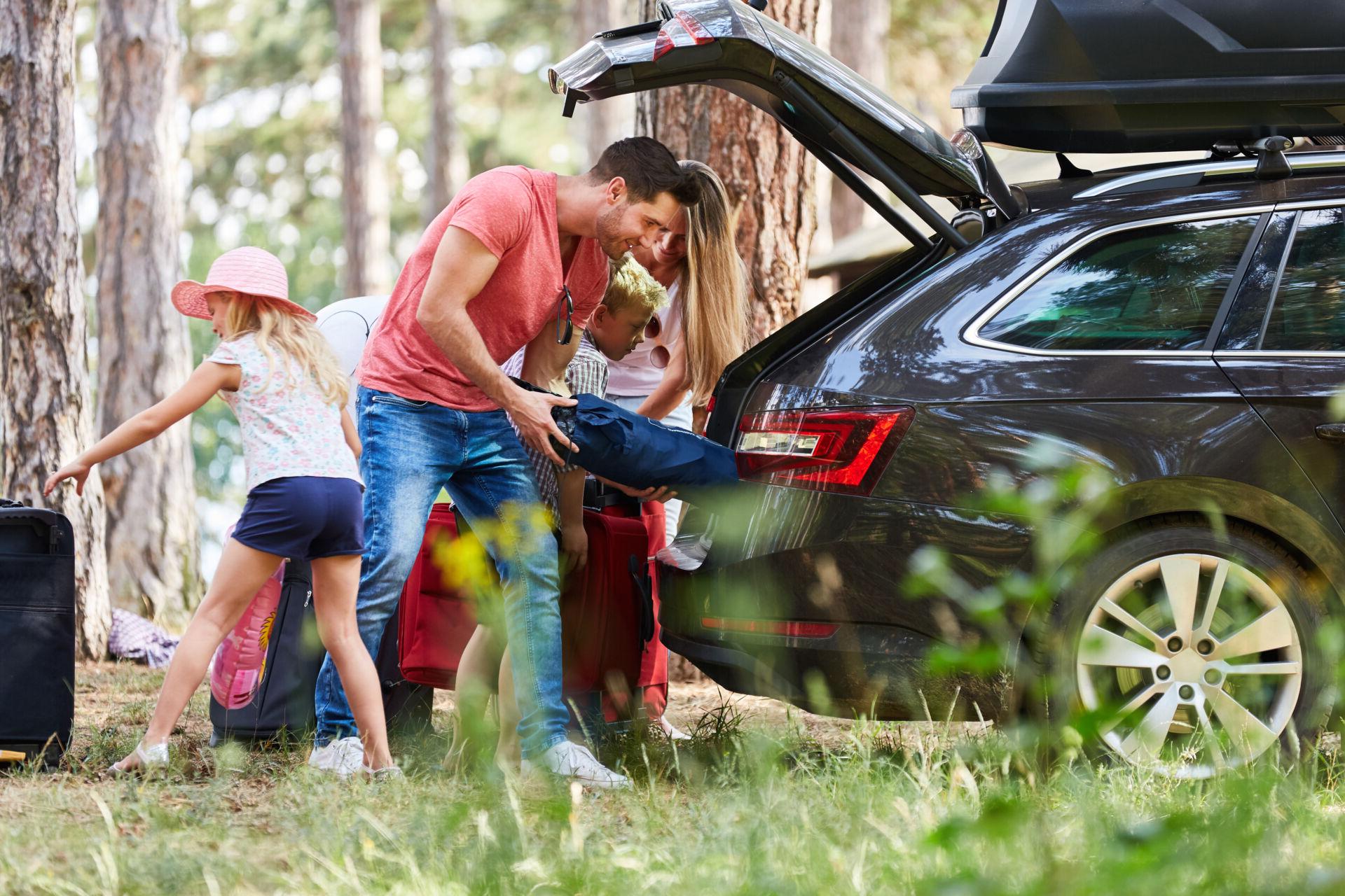 A family unpacks their car at a campsite.